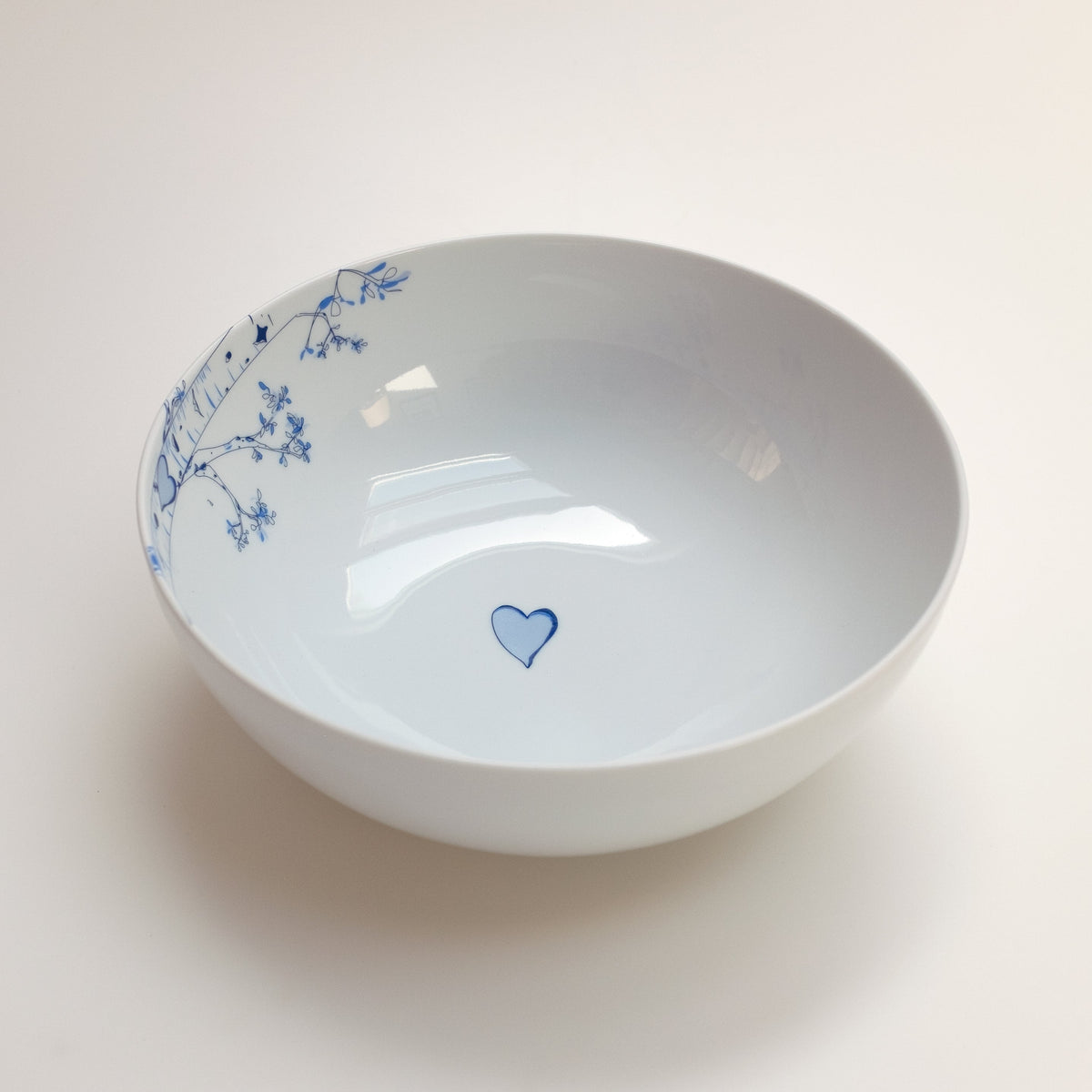 White ceramic bowl with a blue heart design at the center and delicate blue floral patterns along the inner rim on one side.