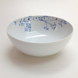 White ceramic serving bowl with delicate blue floral branch patterns decorating the inner rim, shown against a plain white background.