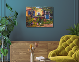 Impressionist-style painting of a yellow house with a blue gate and vibrant garden flowers, displayed on a teal wall above a wooden sideboard and mustard green chair.