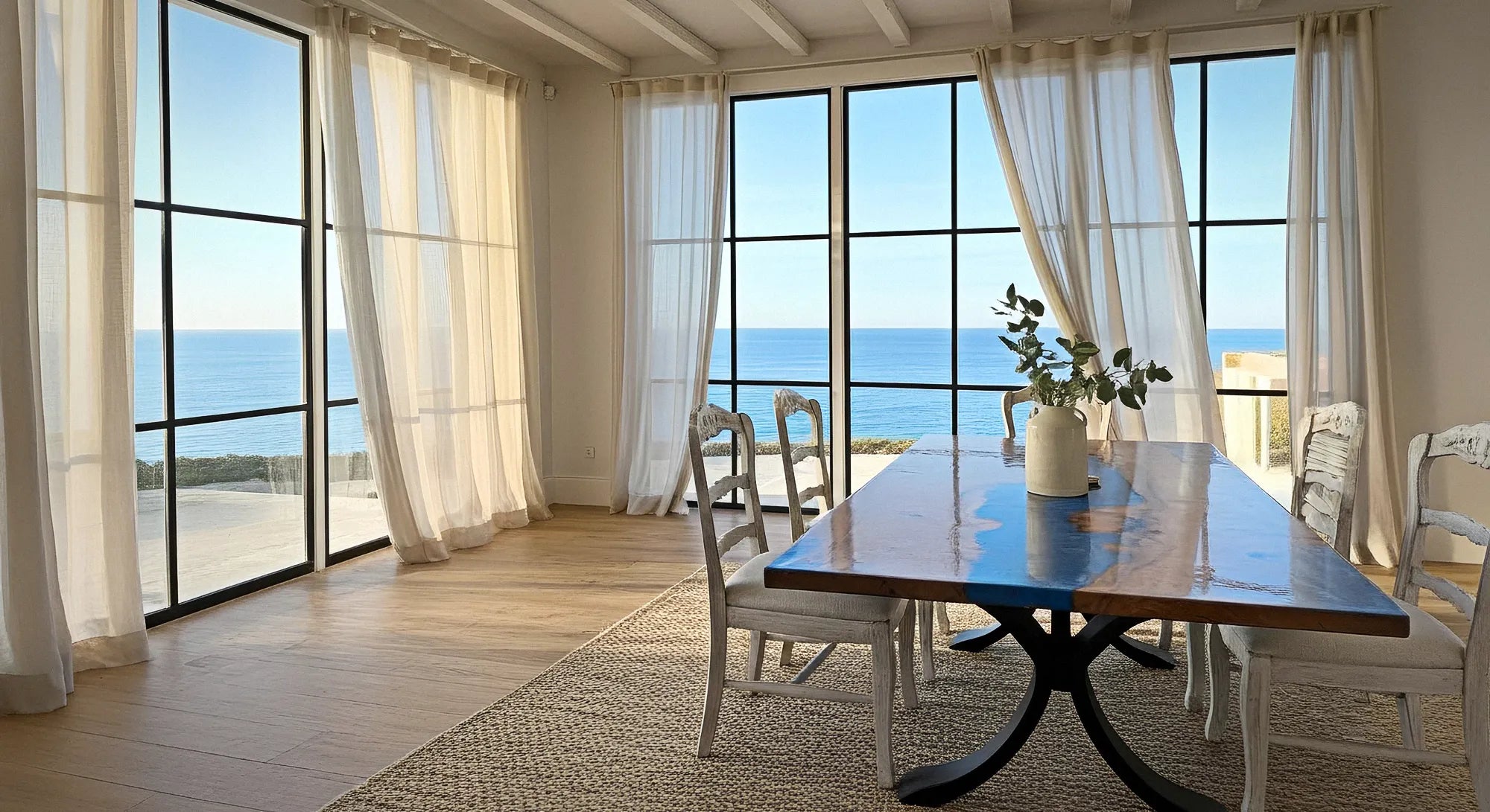 Dining area with a large table and chairs near a large window with a view of the ocean.