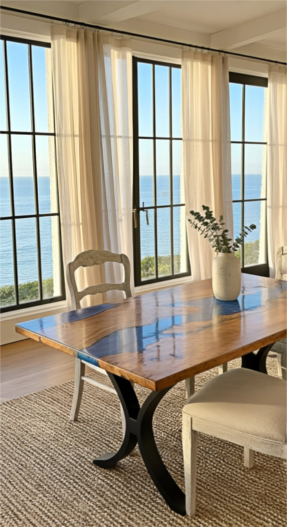 Dining room with wooden table and chairs by large windows overlooking the ocean.
