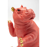 Close-up of a coral pink hippo figurine with detailed skin texture and shiny gold accents on ears, toes, and raised tail against a white background.