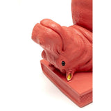 Close-up of a pink hippo bookend lying on its back atop a book-shaped base with a small golden toenail detail on its foot.