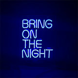Bright blue neon sign displaying the text 'BRING ON THE NIGHT' on a dark background, with evenly spaced uppercase letters arranged in four lines.
