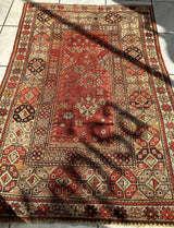 Rectangular antique Turkish prayer rug with distressed red central field featuring geometric floral motifs, surrounded by intricate beige and brown patterned borders and a repeating hexagonal design.