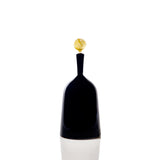 Tall, slender black glass bottle with a narrow neck and a yellow, marbled spherical stopper on top against a white background.