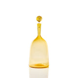Transparent amber glass bottle with a rounded stopper, featuring a wide base and narrow neck, shown against a white background with reflection below.