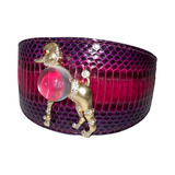 Wide deep purple snakeskin-patterned leather cuff with a gold-tone poodle brooch featuring a large translucent pink orb body and small rhinestone accents.