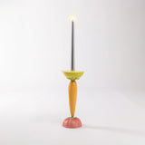 Tall candlestick with a silver candle, featuring a yellow bowl, a carrot-shaped stem, and a red tomato-shaped base on a white background.