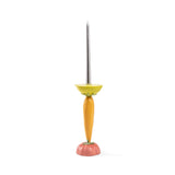 Tall candlestick resembling a carrot with an orange body, green leafy details, a yellow bowl-shaped holder, and a long silver candle placed inside.