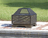 Square metal fire pit with geometric cut-out patterns and mesh hood, placed on a brick patio near a grassy lawn and pool edge