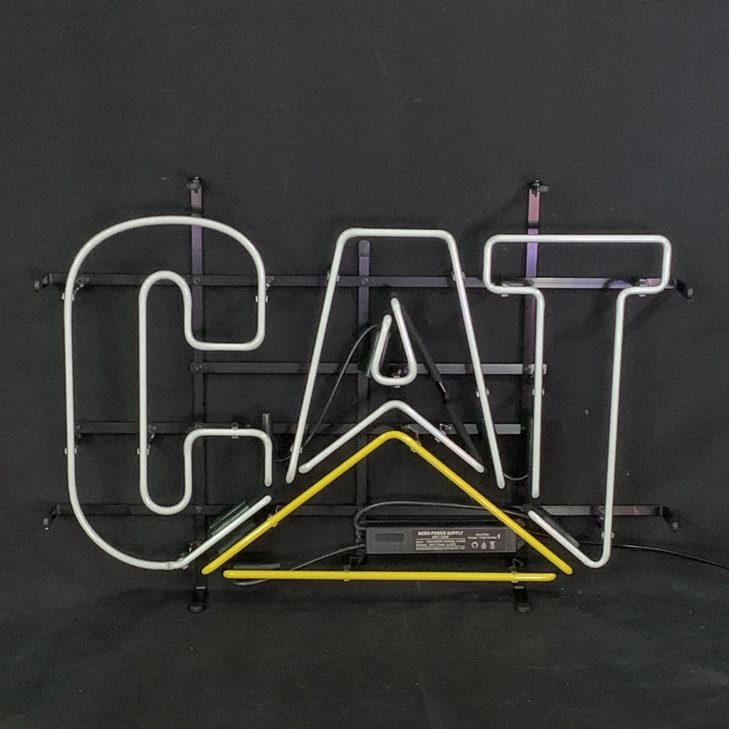 Neon sign spelling 'CAT' with white letters and a yellow triangular underline on a black metal frame against a dark background.