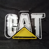 White neon letters spelling 'CAT' with a yellow triangular neon shape beneath the letter A, mounted on a black metal frame
