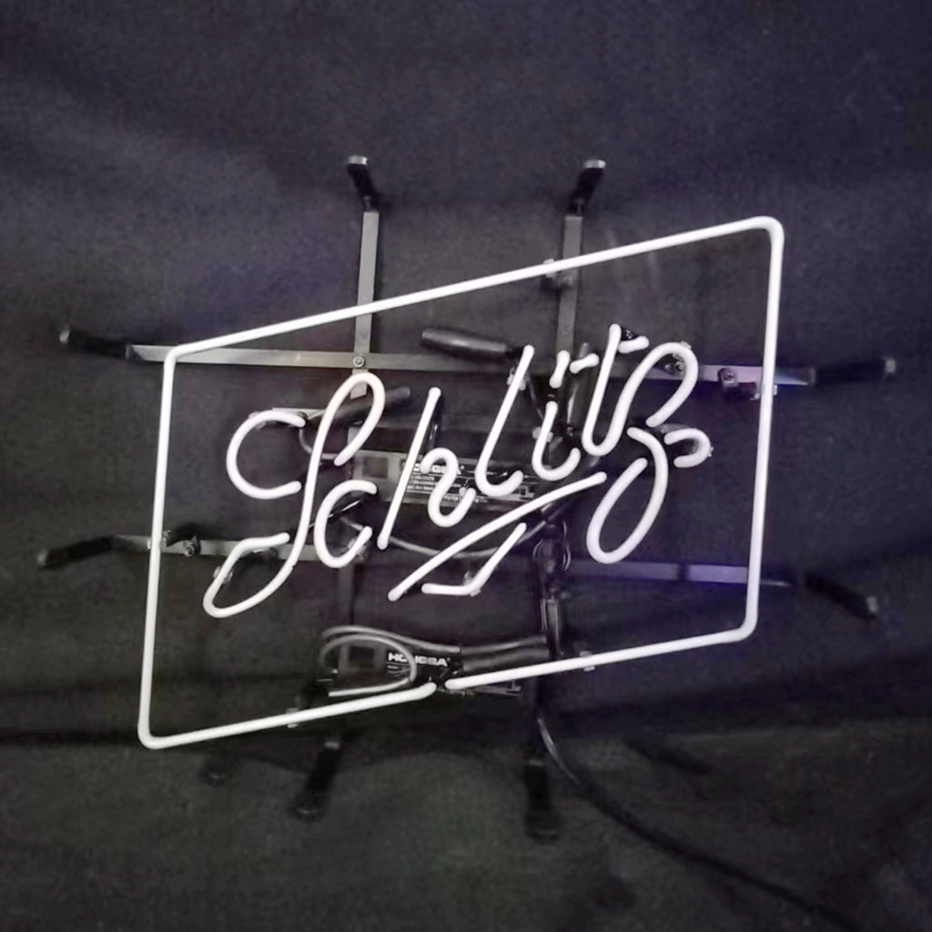 White neon light sign spelling 'Schlitz' in cursive within a tilted rectangular frame against a dark background with support brackets.
