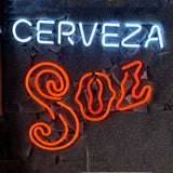 Neon sign with the word CERVEZA in bright white uppercase letters above the stylized SOL in bold, curly red script on a dark textured background.