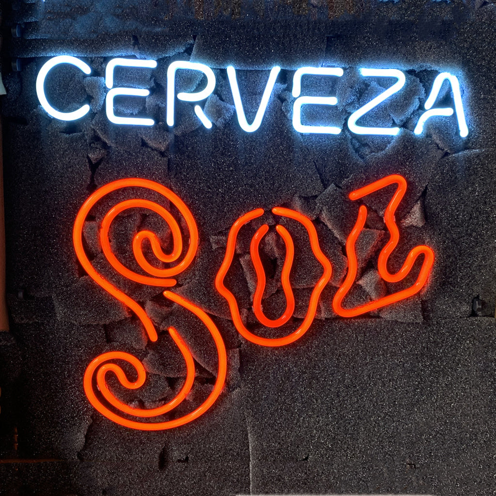 Neon sign with the word CERVEZA in bright white uppercase letters above the stylized SOL in bold, curly red script on a dark textured background.