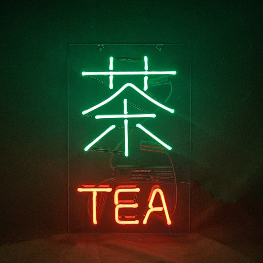 Neon sign featuring a large green Chinese character for tea above the word 'TEA' in red neon letters on a dark background.