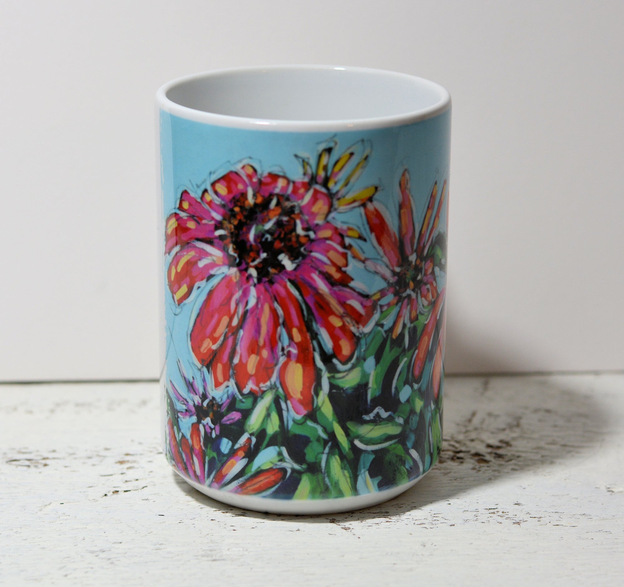 Ceramic mug with Cone Flowers design by Christi Dreese, styled on a table with yellow flowers and dried leaves