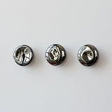 Three polished, round coat hooks with a shiny mercury-like mirror finish mounted in a horizontal row on a white wall.