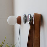 Wall-mounted Sequence coat hooks with polished silver Mercury-style spheres holding a brown leather strap and a brown and white spherical wall lamp nearby.