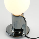 Glossy black ceramic base with organic curved cutout holding a large white frosted glass globe lamp, viewed close-up on a white surface.