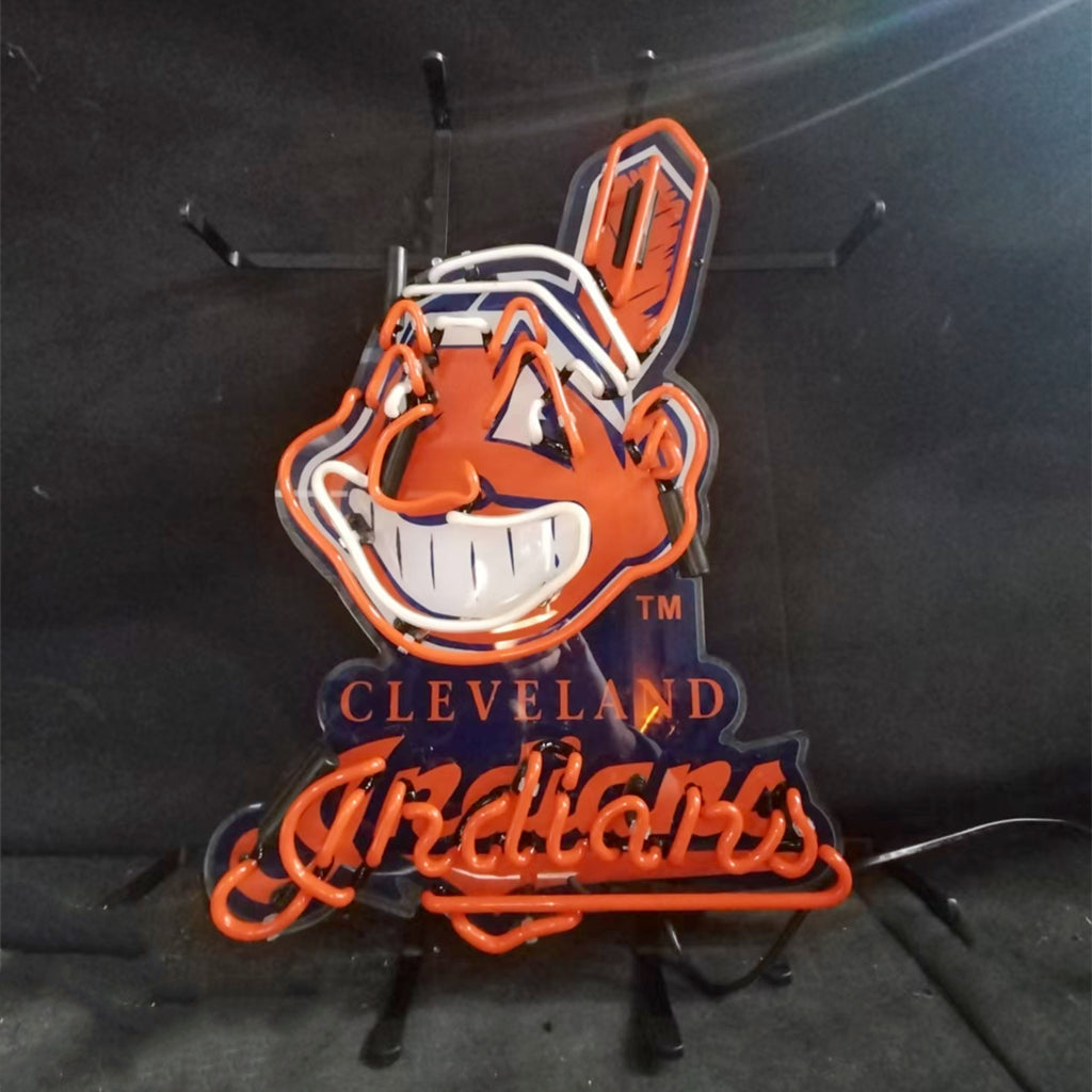 Neon sign depicting the Cleveland Indians mascot with a red face, white teeth, and a feather, above orange neon script reading 'Indians' on a dark background.
