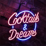 Neon sign with pink cursive text reading 'Cocktails & Dreams' surrounded by a blue circular outline against a dark brick wall background.