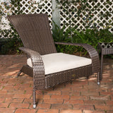 Brown synthetic wicker outdoor lounge chair with wide curved arms and a thick beige cushion on a brick patio, set against a white lattice fence with greenery behind.