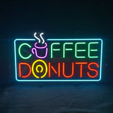 Bright neon sign with the word 'COFFEE' in green and pink above 'DONUTS' in red and yellow, featuring a steaming coffee cup and a donut illustration inside a blue rectangular border.