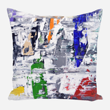 Square pillow with abstract brushstroke design featuring scattered patches of green, blue, orange, red, yellow, and neutral gray on a primarily white and gray background.
