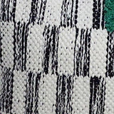 Close-up of a handwoven pillow fabric with white and black textured geometric stripes and a green accent in the corner.