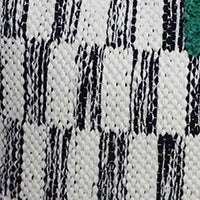 Close-up of a handwoven pillow fabric with white and black textured geometric stripes and a green accent in the corner.