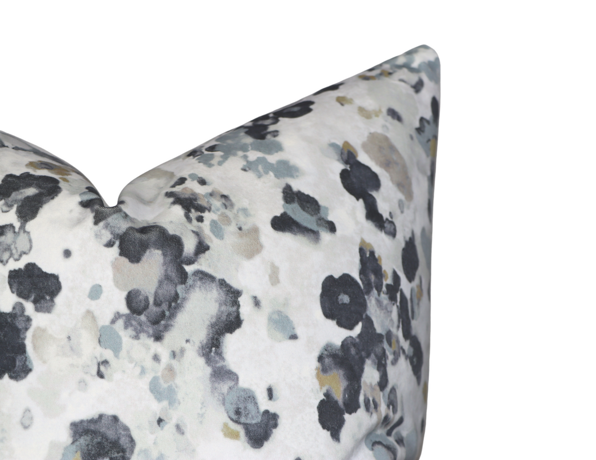 Close-up of a velvet pillow cover with an abstract, mottled pattern in black, gray, and beige on a white background