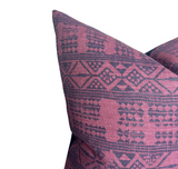 Close-up of a square pillow cover showing a tribal-inspired geometric pattern in deep red and dark blue hues.