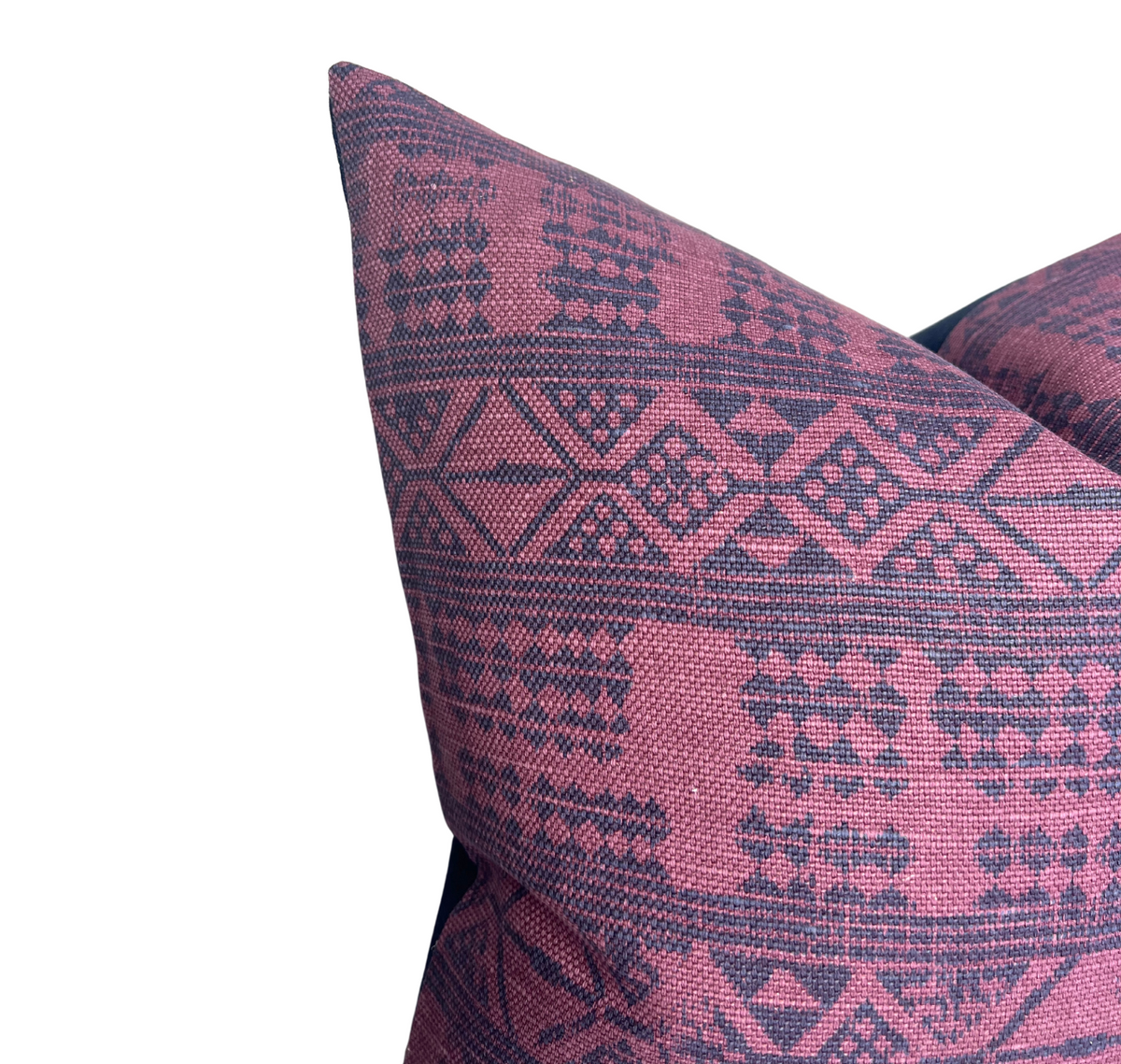 Close-up of a square pillow cover showing a tribal-inspired geometric pattern in deep red and dark blue hues.