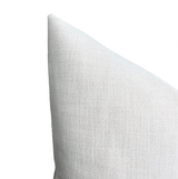 Close-up of a triangular corner of a chalk-colored woven outdoor pillow cover with a textured fabric surface.