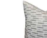 Close-up of a pillow covered in fabric with horizontal irregular gray stripes on a soft off-white background, angled to show the pillow's top corner.