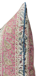 Corner of a decorative pillow with pink and cream floral patterns, featuring contrasting dark blue piping along the edge for a defined finish.
