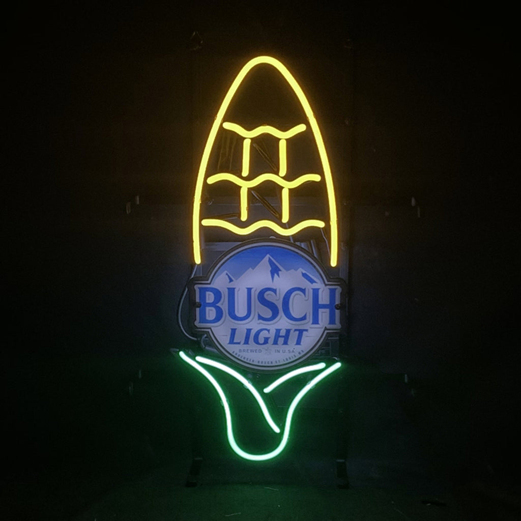 Neon sign shaped like an ear of corn with yellow kernels and green husk surrounding a blue and white Busch Light beer logo at the center, mounted on a black background.