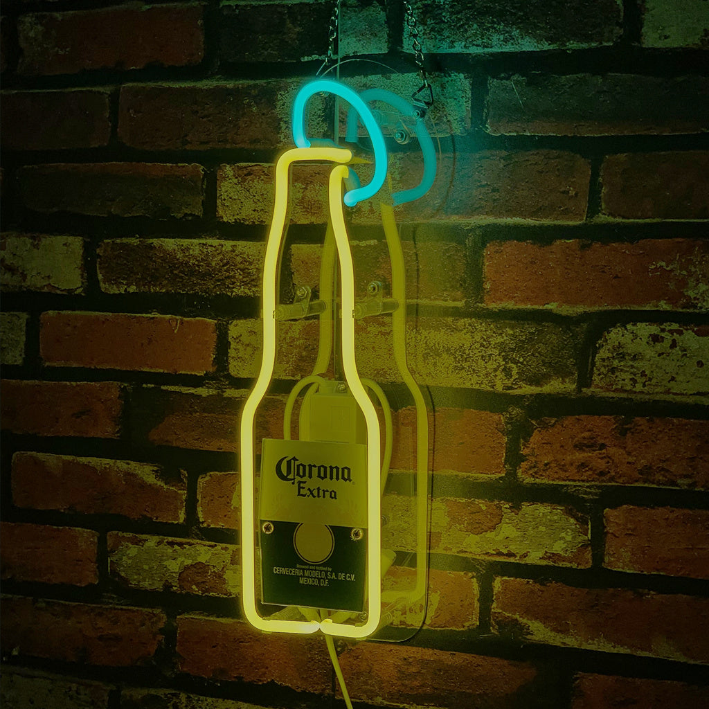 Yellow neon outline of a Corona Extra beer bottle with a blue neon lime slice above it, mounted on a red and brown brick wall, casting a shadow.