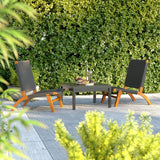 Two modern lounge chairs with curved wooden frames and black woven seats placed around a square black table on a gray tiled patio, with dense green foliage background.