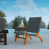 Outdoor lounge chair with curved wooden legs and dark woven back and seat, positioned on a concrete patio beside a small matching side table holding a glass decanter and glass.