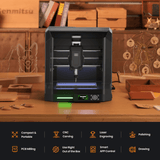 Compact black desktop CNC router with transparent front panel on wooden workbench surrounded by wooden crafts and tools against a workshop background.