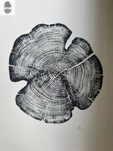 Black woodcut print of a cedar tree ring cross-section showing detailed growth rings and natural cracks on white background.