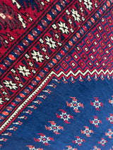 Close-up of a vintage Yagcibedir Turkish wool prayer rug with red and deep blue fields featuring geometric cream and red motifs and intricate border patterns.