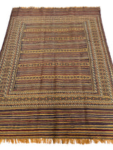 Rectangular wool kilim rug with geometric patterns in warm earth tones and stripes, featuring detailed borders and short fringes on narrow edges.
