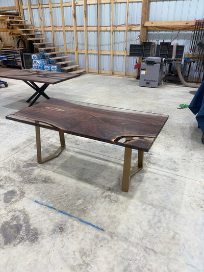 Handcrafted walnut slab table with clear resin finish and gold legs in a workshop setting