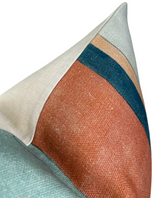 Close-up of a rectangular pillow cover featuring color blocks in apricot, teal, and beige with a visible seam and textured fabric detail.