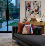 Dark gray chaise lounge with two colorful pillows, one in solid rust claret and another geometric with claret, navy, blush, and cream, set in a modern living room with abstract art.