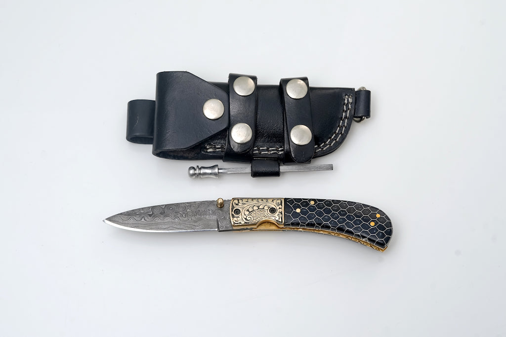 Hand-Engraved Damascus Folding Knife with Honeycomb Handle laid open on dark surface